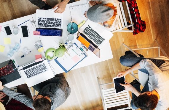 Young developers working in their start-up home office. They are brainstorming, woman holding pencil and writing while talking with her coworker. They are collaborating. Top view. Location is released.